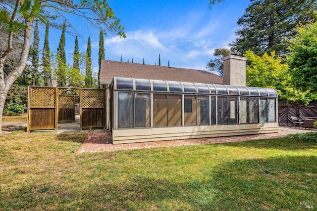 rear view of property with roof with shingles, fence, a sunroom, a chimney, and a yard