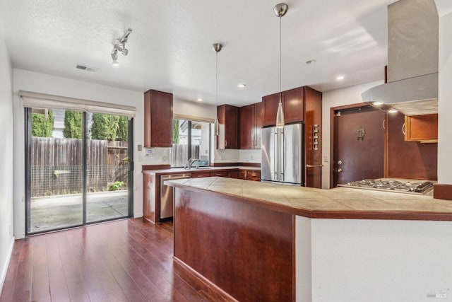 kitchen featuring decorative light fixtures, island range hood, appliances with stainless steel finishes, visible vents, and a sink
