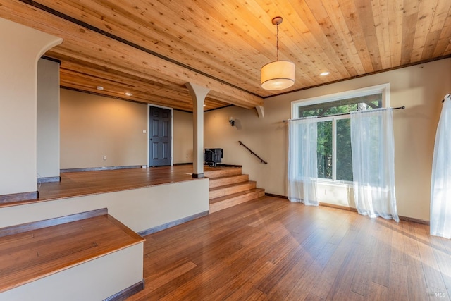 unfurnished living room featuring baseboards, wood finished floors, stairs, and wooden ceiling