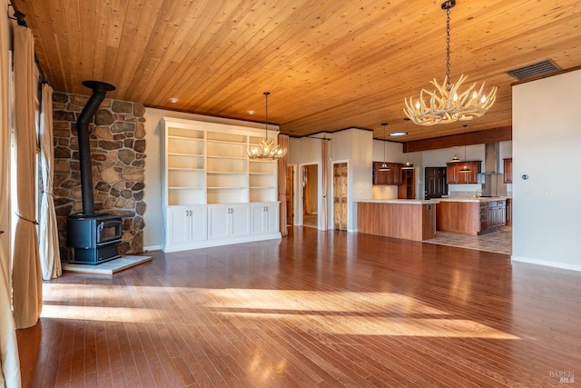 unfurnished living room featuring hardwood / wood-style flooring, a wood stove, wooden ceiling, and a notable chandelier