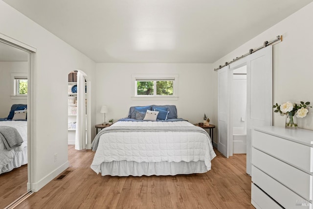 bedroom featuring arched walkways, baseboards, light wood-type flooring, and visible vents