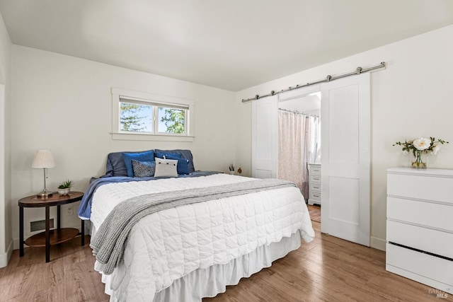 bedroom featuring a barn door, baseboards, wood finished floors, and visible vents