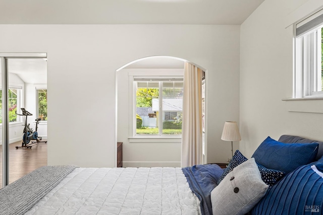 bedroom with arched walkways, wood finished floors, and multiple windows