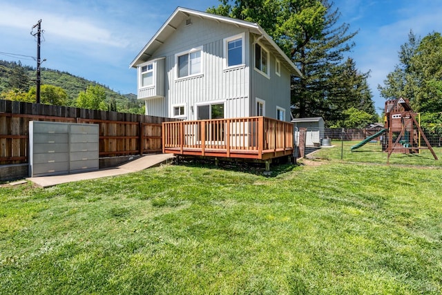 back of house with a wooden deck, a fenced backyard, a shed, a playground, and an outbuilding