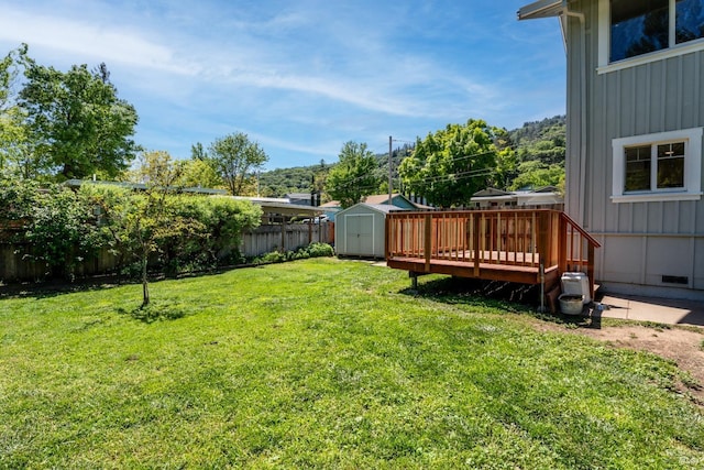view of yard featuring a storage unit, a fenced backyard, a deck, and an outdoor structure