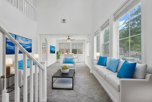 carpeted living area with baseboards, visible vents, a ceiling fan, and a high ceiling