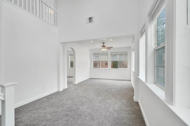 interior space with ceiling fan, baseboards, arched walkways, carpet floors, and a towering ceiling