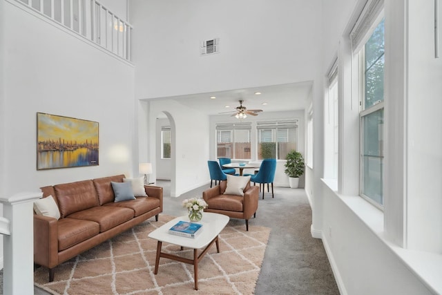 carpeted living area with arched walkways, ceiling fan, baseboards, visible vents, and a high ceiling