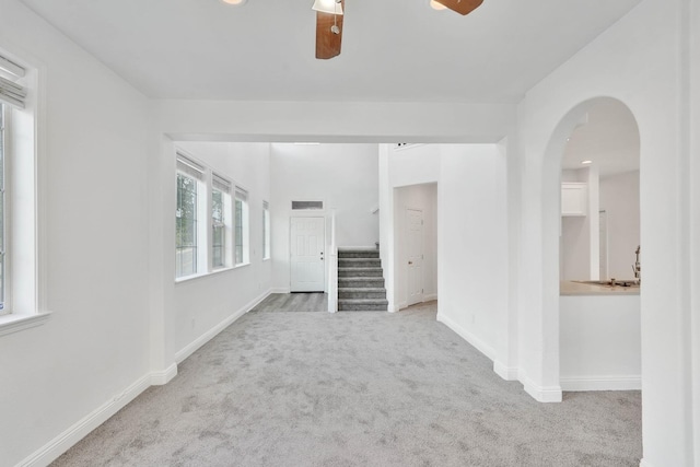 unfurnished living room with stairs, ceiling fan, carpet, and baseboards