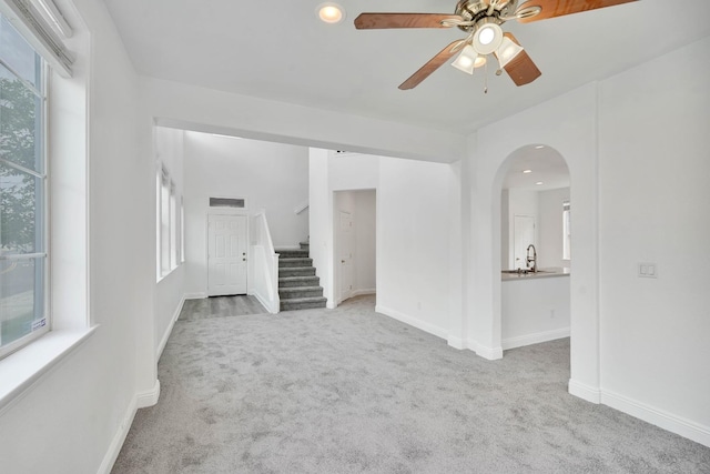 carpeted spare room featuring a sink, stairway, ceiling fan, and plenty of natural light