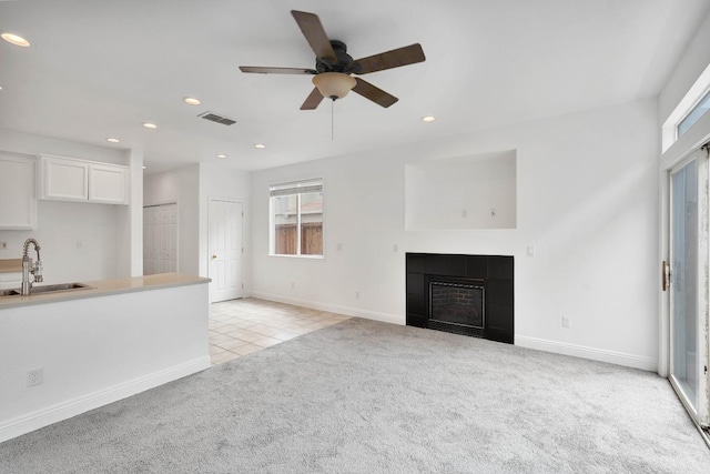unfurnished living room featuring a sink, a tiled fireplace, ceiling fan, visible vents, and light carpet