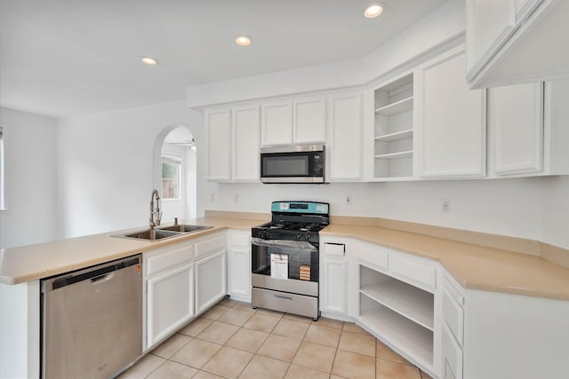 kitchen with a sink, open shelves, a peninsula, arched walkways, and appliances with stainless steel finishes