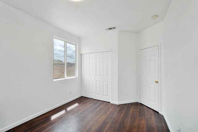 unfurnished bedroom featuring dark wood finished floors, visible vents, a closet, and baseboards
