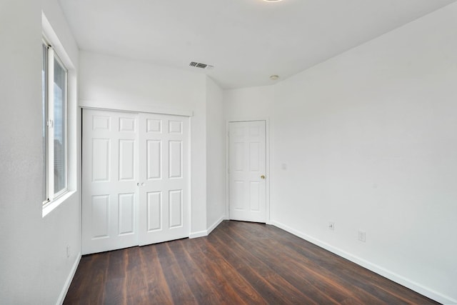 unfurnished bedroom featuring dark wood finished floors, visible vents, a closet, and baseboards