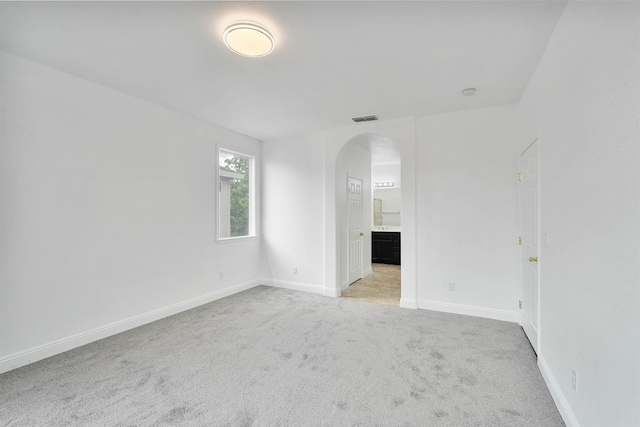 spare room with baseboards, visible vents, arched walkways, and light carpet