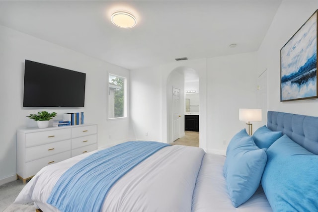bedroom featuring light colored carpet, visible vents, baseboards, arched walkways, and ensuite bath