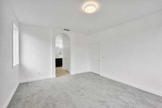 carpeted spare room featuring baseboards, visible vents, and arched walkways