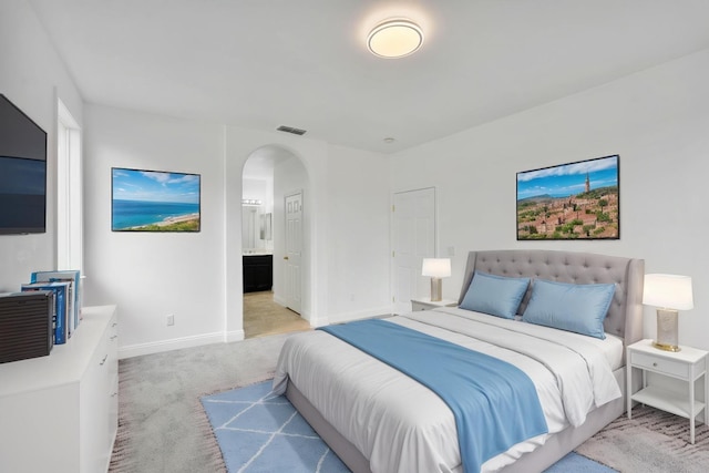 carpeted bedroom featuring visible vents, ensuite bathroom, baseboards, and arched walkways