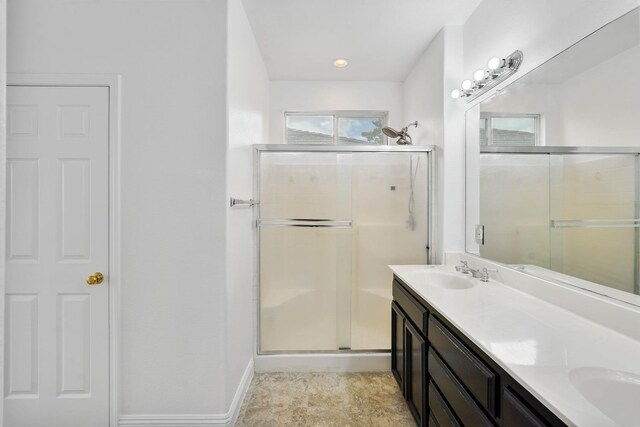 bathroom with double vanity, a shower stall, baseboards, and a sink