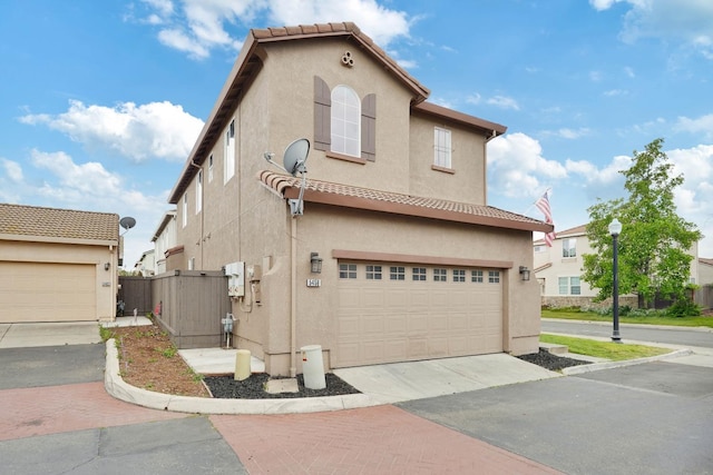 view of side of property featuring an attached garage, driveway, stucco siding, and fence