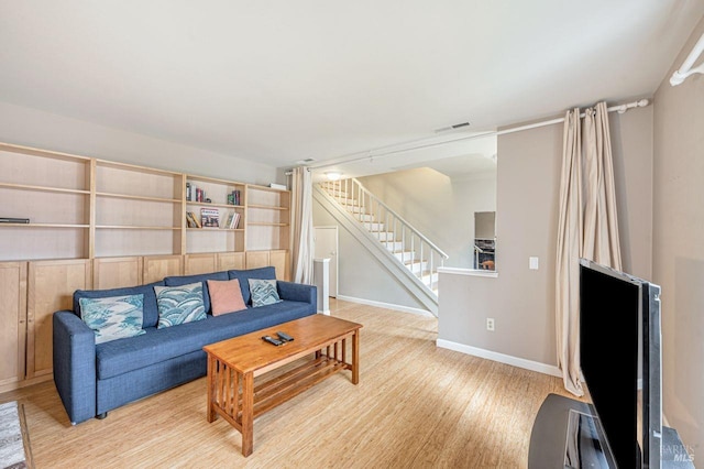 living room with baseboards, visible vents, stairway, and light wood-type flooring