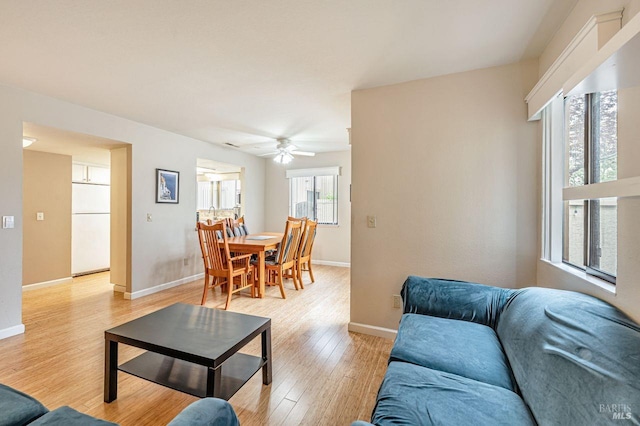living room with baseboards, ceiling fan, and light wood-style flooring