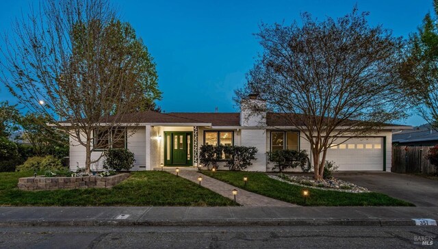 ranch-style home featuring a chimney, a front lawn, driveway, fence, and a garage
