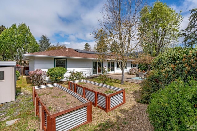 back of property featuring roof mounted solar panels, a garden, and roof with shingles