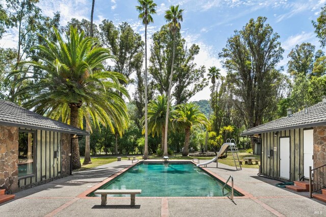 outdoor pool with a water slide, a diving board, and a patio
