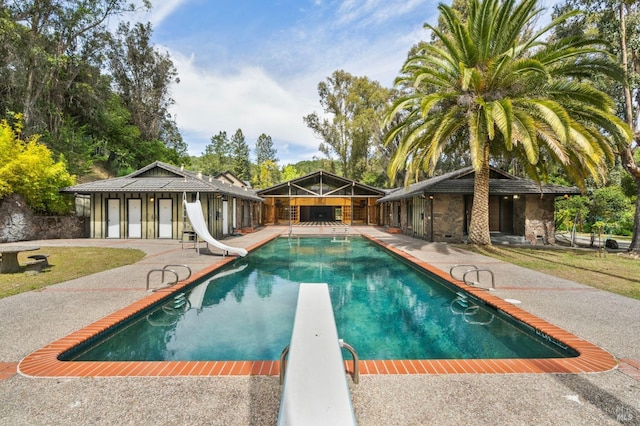 pool featuring a patio area, a water slide, and a diving board