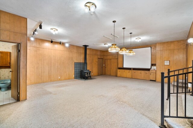 unfurnished living room with light colored carpet, track lighting, wood walls, and a wood stove