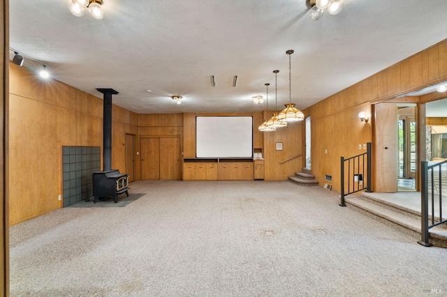 unfurnished living room with stairway, wood walls, a wood stove, and light colored carpet