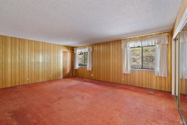 unfurnished room featuring carpet floors, a textured ceiling, wood walls, and visible vents