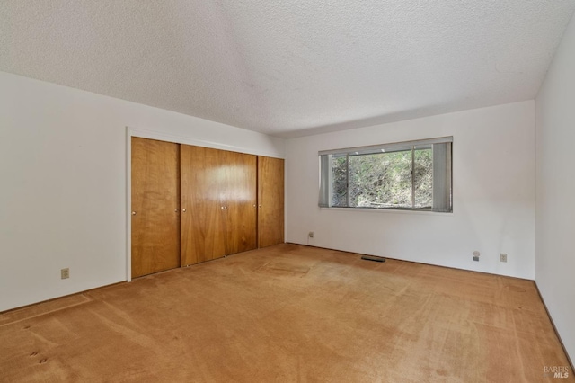 unfurnished bedroom featuring carpet flooring, a textured ceiling, visible vents, and a closet