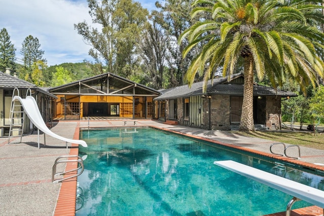 pool featuring a water slide, a diving board, and a patio