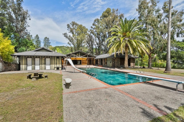 pool featuring a patio area, a water slide, a lawn, and a diving board