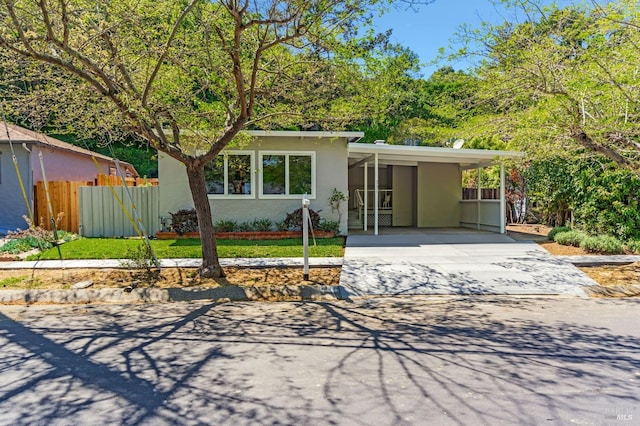 view of front facade with concrete driveway, fence, an attached carport, and stucco siding