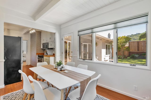 dining space with beamed ceiling, light wood finished floors, and baseboards