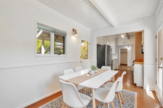dining room featuring baseboards, a healthy amount of sunlight, beam ceiling, and light wood-type flooring