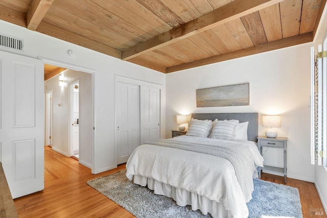 bedroom with light wood finished floors, beamed ceiling, a closet, baseboards, and wood ceiling