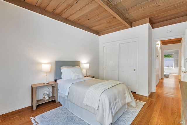 bedroom with a closet, light wood-type flooring, beamed ceiling, wooden ceiling, and baseboards