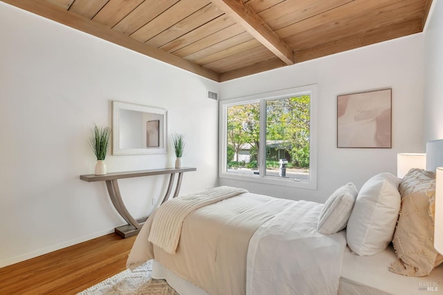 bedroom featuring wood finished floors, beamed ceiling, wooden ceiling, baseboards, and visible vents