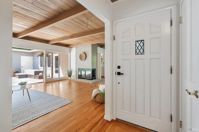entrance foyer with wood ceiling, a brick fireplace, beam ceiling, and light wood-style floors
