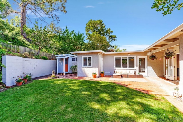 back of house with outdoor lounge area, a fenced backyard, a yard, stucco siding, and an outdoor structure