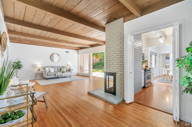 living area featuring wood ceiling, a brick fireplace, beam ceiling, and light wood finished floors