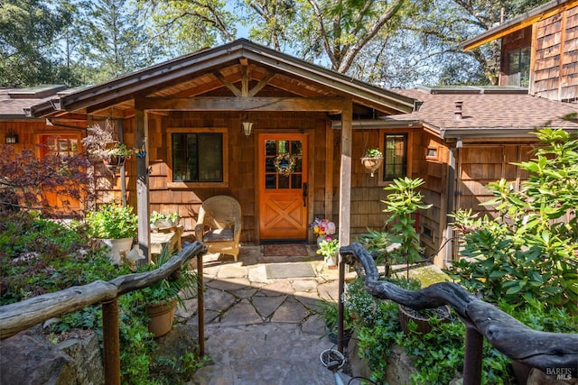 doorway to property featuring covered porch and roof with shingles
