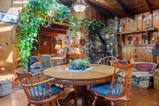 dining area with lofted ceiling with beams, wooden ceiling, wood finished floors, wooden walls, and a wood stove