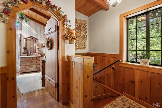 stairway with wood-type flooring, a healthy amount of sunlight, vaulted ceiling with beams, and wainscoting