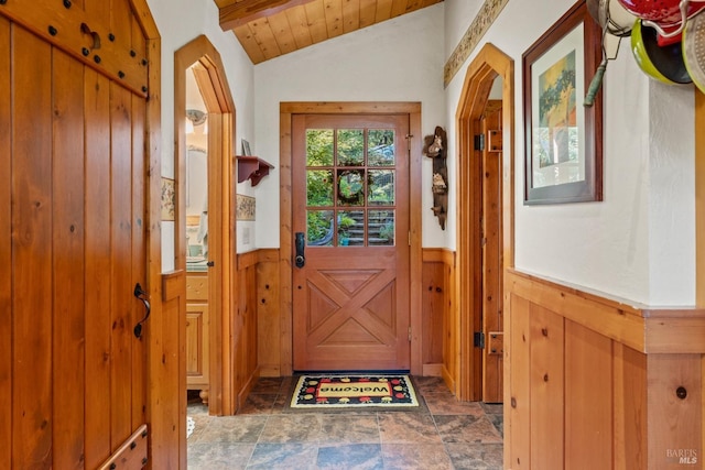 doorway to outside with a wainscoted wall, wood walls, stone finish flooring, and vaulted ceiling
