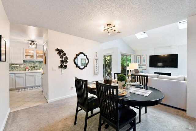 dining space featuring light carpet, a textured ceiling, light tile patterned flooring, baseboards, and vaulted ceiling with skylight